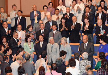 聴衆の盛大な拍手に迎えられご着席する両陛下の写真 聴衆の盛大な拍手に迎えられご着席する両陛下の写真