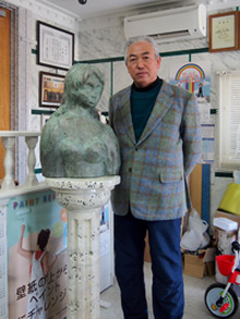 本物以上を目指した石柱と銅像と写る木暮さんの画像