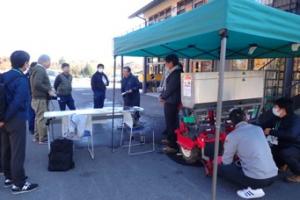 屋外での大型機械の展示と説明の様子の写真